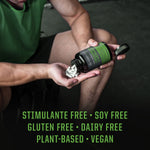 Person in green athletic wear pouring white capsules from a black bottle labeled with green text into their palm, with overlay text highlighting stimulant free, soy free, gluten free, dairy free, plant-based, and vegan attributes.