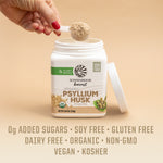 Hand holding a scoop of light brown psyllium husk powder above an open white container on beige background