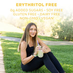 Woman in black activewear sitting on grass drinking a lemon-colored beverage outdoors in sunlight