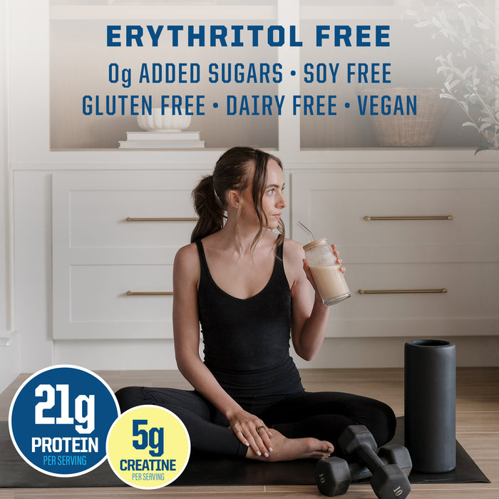 Woman in black workout clothes sitting on a mat drinking protein shake next to weights and foam roller