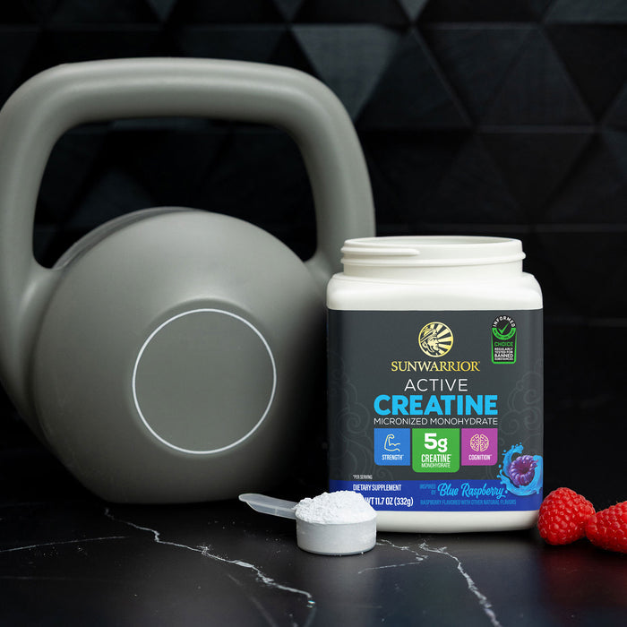 Sunwarrior creatine container with scoop of white powder, kettlebell, and raspberries on black surface