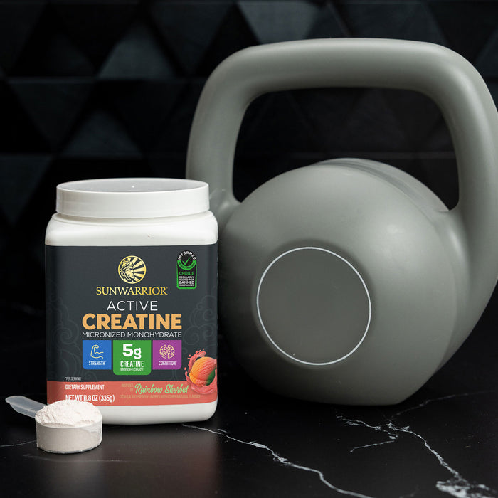Container of Sunwarrior active creatine powder next to a grey kettlebell on a dark surface