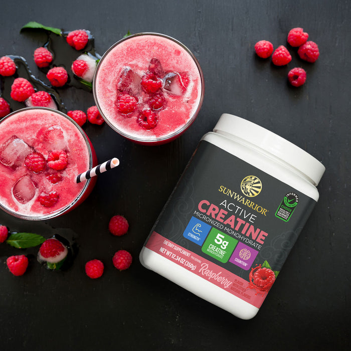 Container of Sunwarrior creatine powder beside two raspberry smoothies with ice on black surface