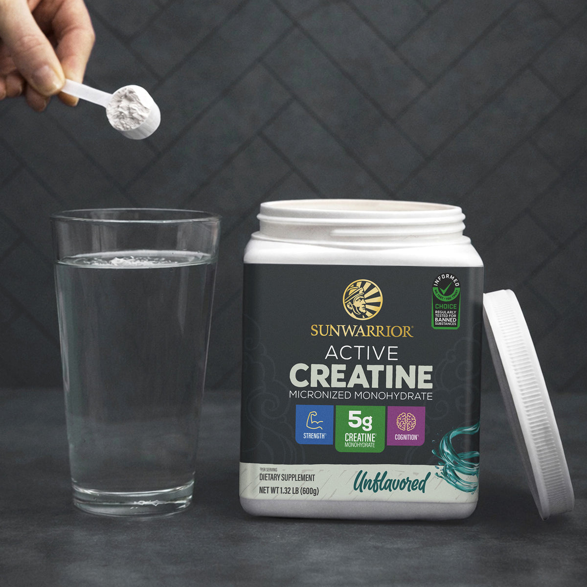 Sunwarrior Active Creatine container with scoop of powder above glass of water on dark surface