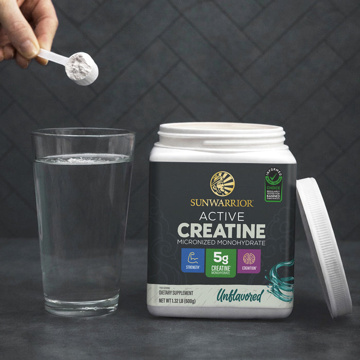 Sunwarrior Active Creatine container with scoop of powder above glass of water on dark surface