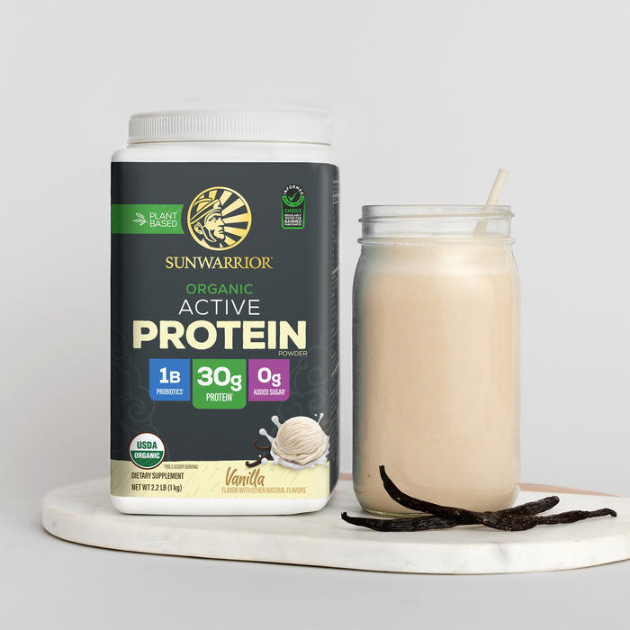 Container of organic vanilla plant-based protein powder next to a glass of creamy vanilla shake with vanilla beans