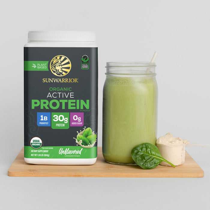 Container of Sunwarrior Organic Active Protein powder next to a green smoothie with spinach leaf and scoop on wood board