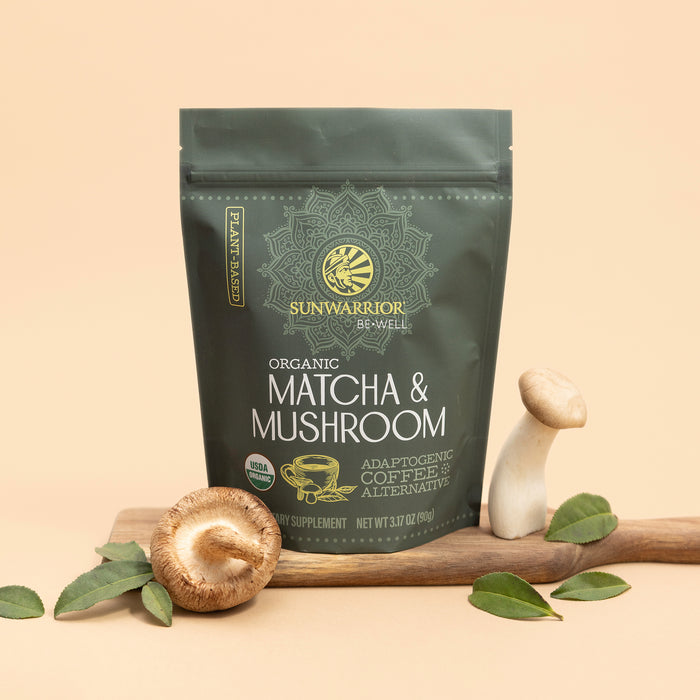 Sunwarrior organic matcha and mushroom powder supplement pouch with fresh mushrooms and green leaves on wood