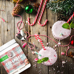 Two peppermint-flavored smoothies with candy canes, near protein powder and holiday decorations on wood