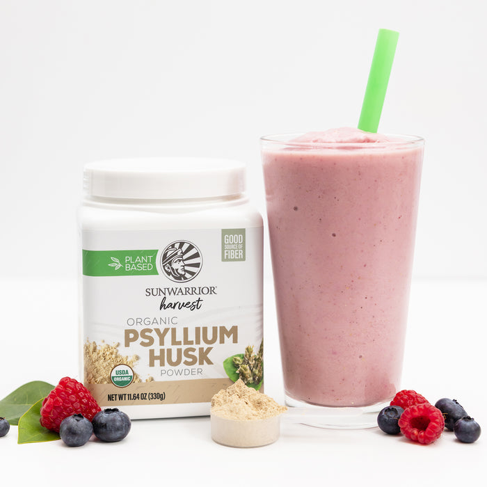 Container of organic psyllium husk powder with a pink smoothie and fresh berries on white background