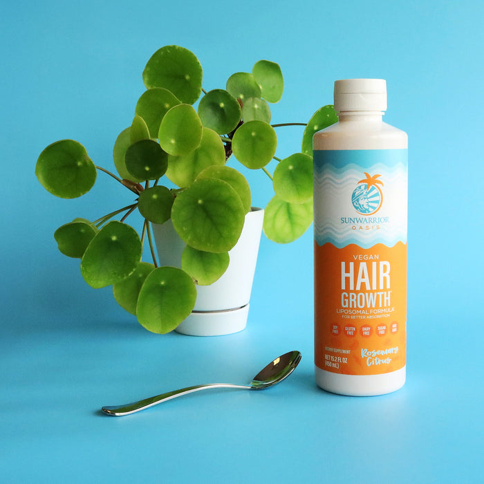 Bottle of vegan hair growth formula with rosemary citrus flavor next to green potted plant and spoon