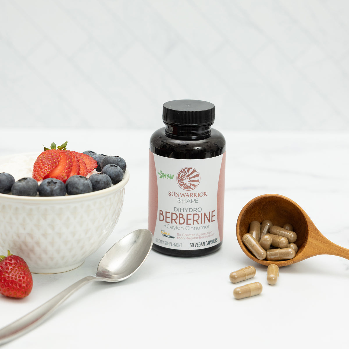 Bottle of Berberine capsules next to a spoon, wooden scoop with capsules, and a bowl of berries and yogurt