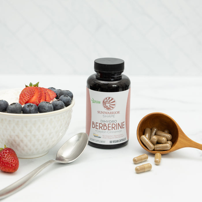 Bottle of Berberine capsules next to a spoon, wooden scoop with capsules, and a bowl of berries and yogurt