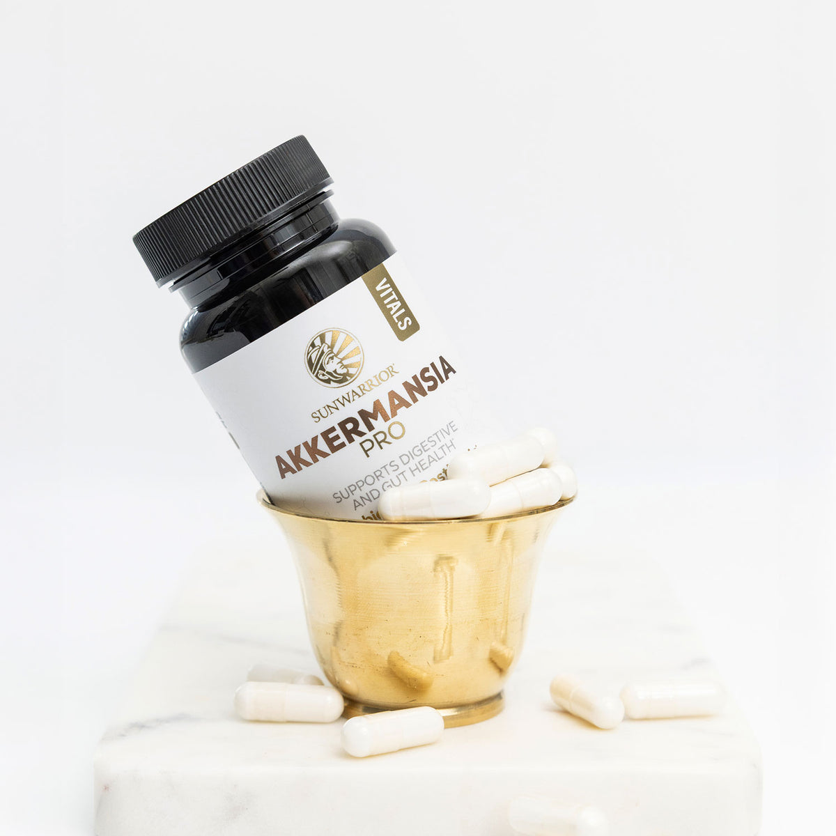 Bottle of Akkermansia Pro capsules in a gold cup with white capsules scattered on a marble surface