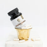 Bottle of Akkermansia Pro capsules in a gold cup with white capsules scattered on a marble surface
