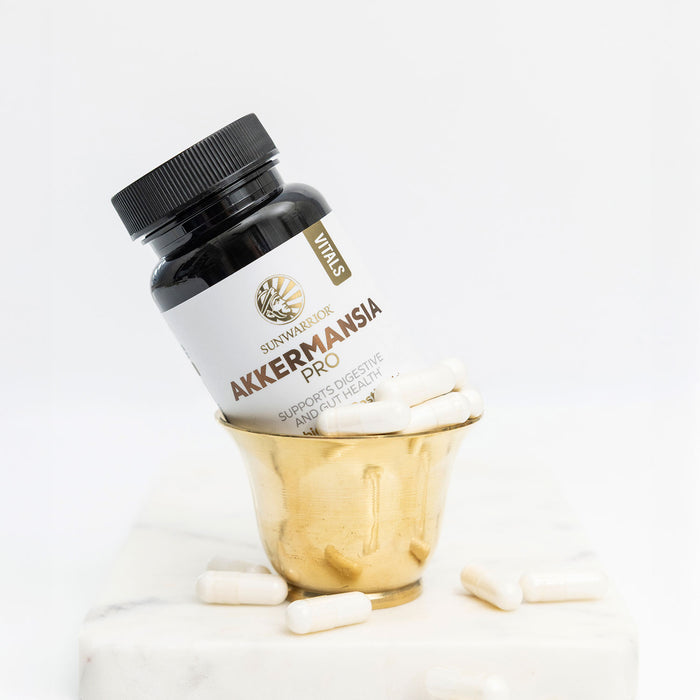 Bottle of Akkermansia Pro capsules in a gold cup with white capsules scattered on a marble surface
