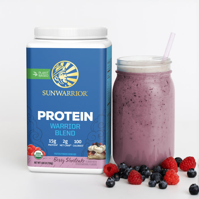 Container of plant-based protein powder next to a berry smoothie in a glass jar with fresh berries scattered around