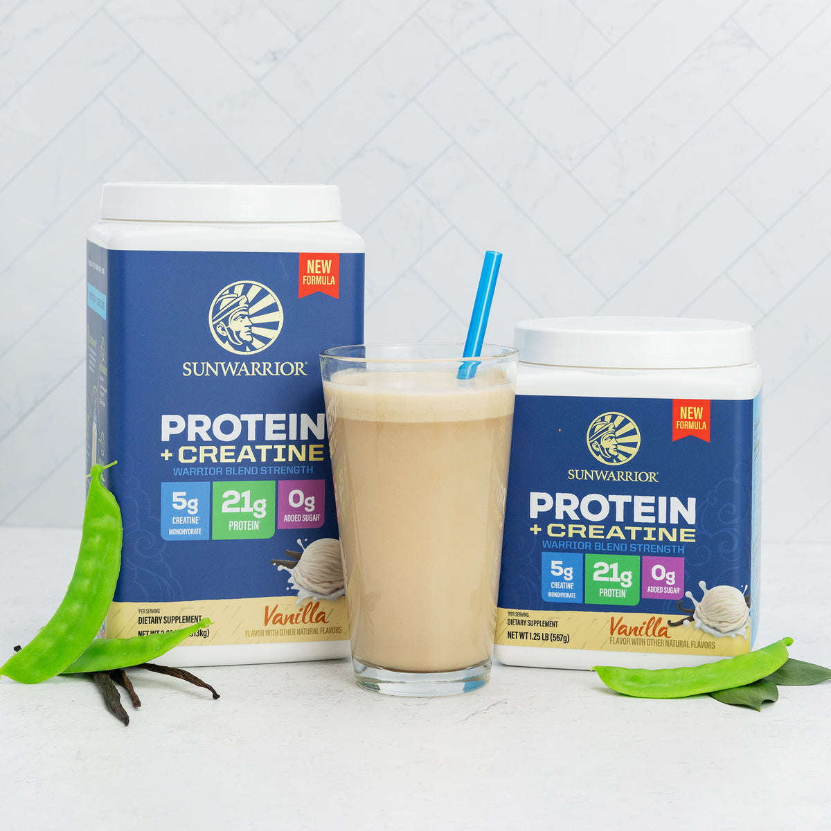 Two containers of vanilla plant-based protein powder and creatine by Sunwarrior with a vanilla smoothie in a glass and green leaves nearby