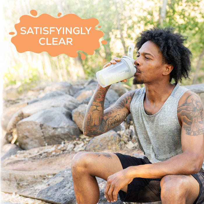 Man with tattoos drinking a clear protein shake outdoors with 