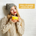 Woman in a knit sweater and hat holding a yellow mug with fall flavor text on a white brick wall