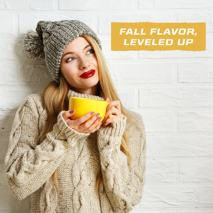 Woman in a knit sweater and hat holding a yellow mug with fall flavor text on a white brick wall