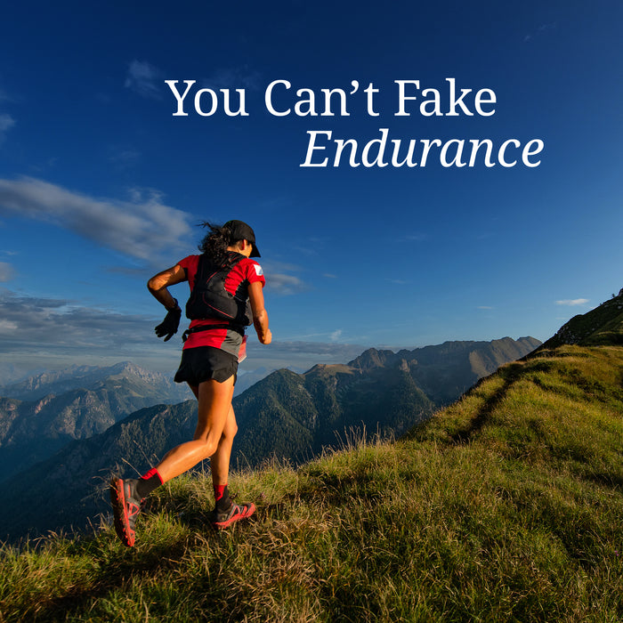 Runner wearing red and black gear ascends a grassy mountain trail under a clear blue sky with text about endurance