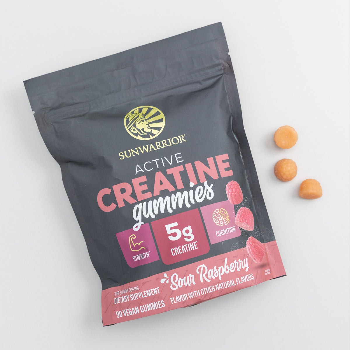 Black and pink pouch of Sunwarrior creatine gummies with three orange gummies beside it