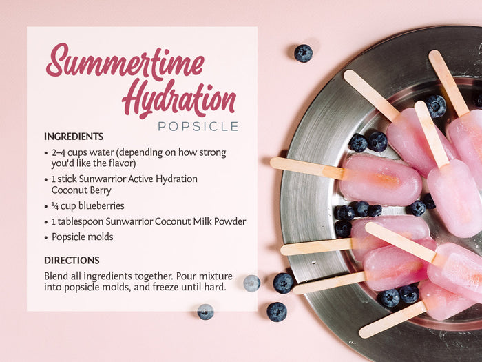 Popsicles on a plate with blueberries and a recipe card for a coconut berry hydration popsicle.