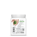 White container of green goddess matcha smoothie with handwritten recipe and hand holding green leaves on label